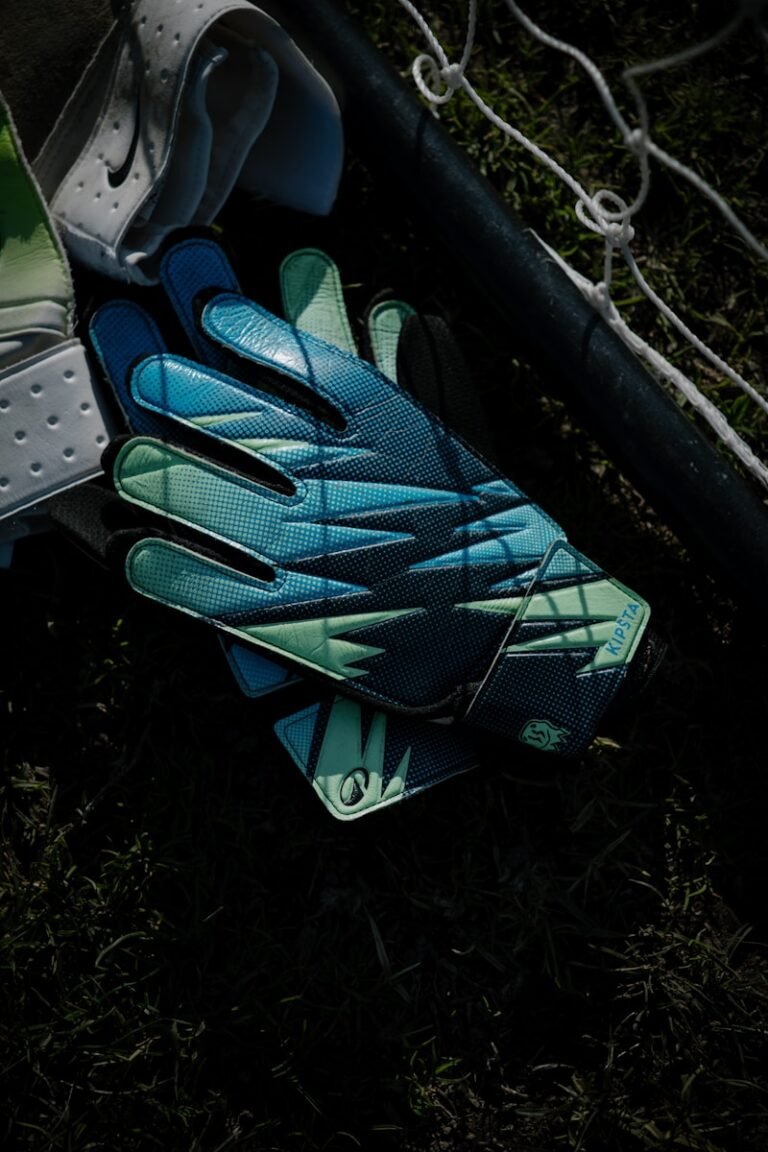 youth goalie gloves resting on grass near a net.