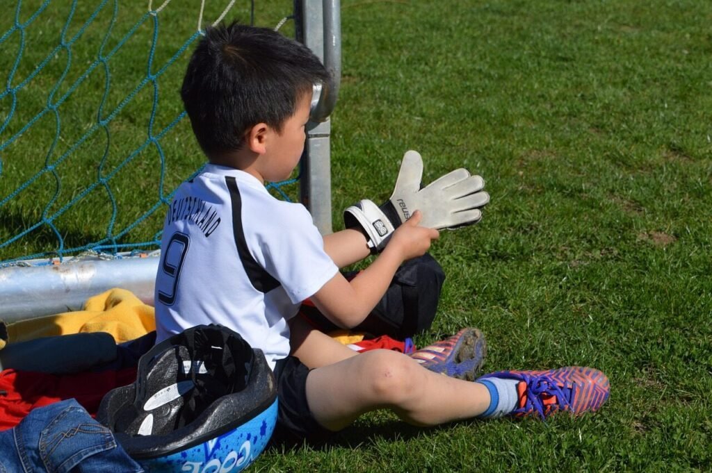  a young child wearing youth goalie gloves on a soccer field .