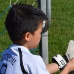 a young child wearing youth goalie gloves on a soccer field .
