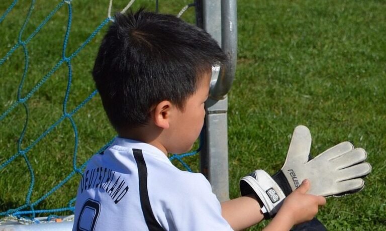 a young child wearing youth goalie gloves on a soccer field .