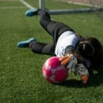 young girl wearing youth goalie gloves and playing soccer on green grass field during