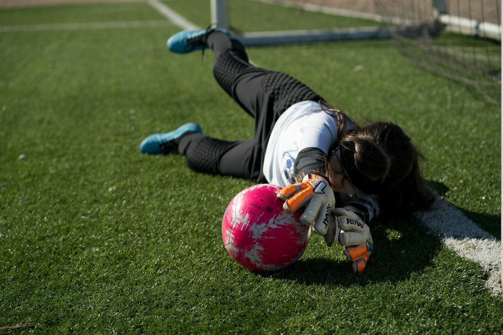 young girl wearing youth goalie gloves and playing soccer on green grass field during