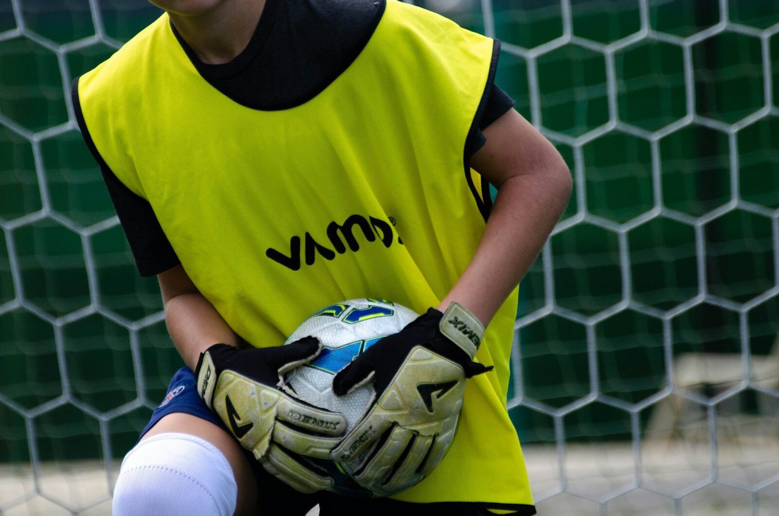 a young boy wearing youth goalie gloves and holding soccer ball in front of a net